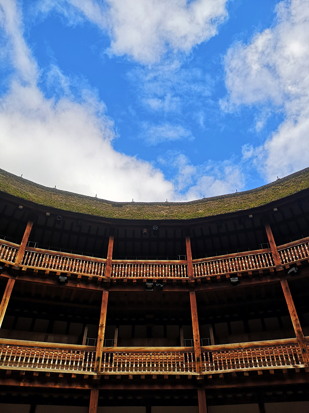 Spring Globe Theatre Reopening 2021 A bright blue sky, with streaks of clouds, above the timber tiered galleries of the Globe Theatre.