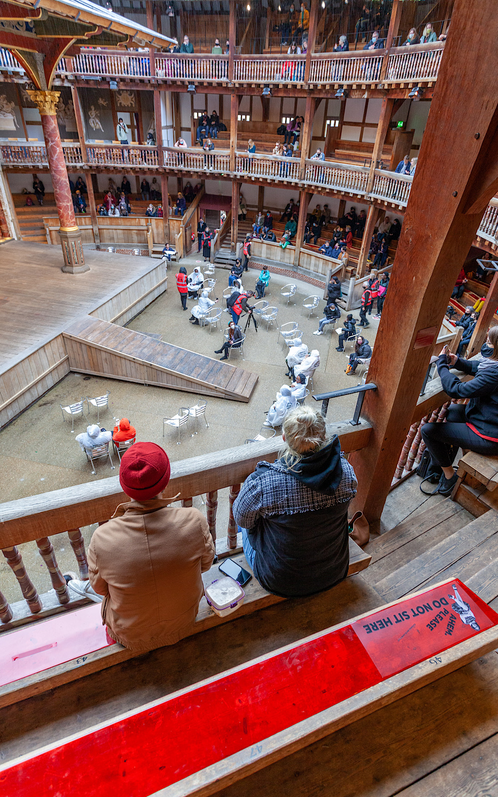 Covid Coronavirus Shakespeare’s Globe Pete Le May 2021 Two people sit on a bench in the balcony of an outdoor wooden theatre