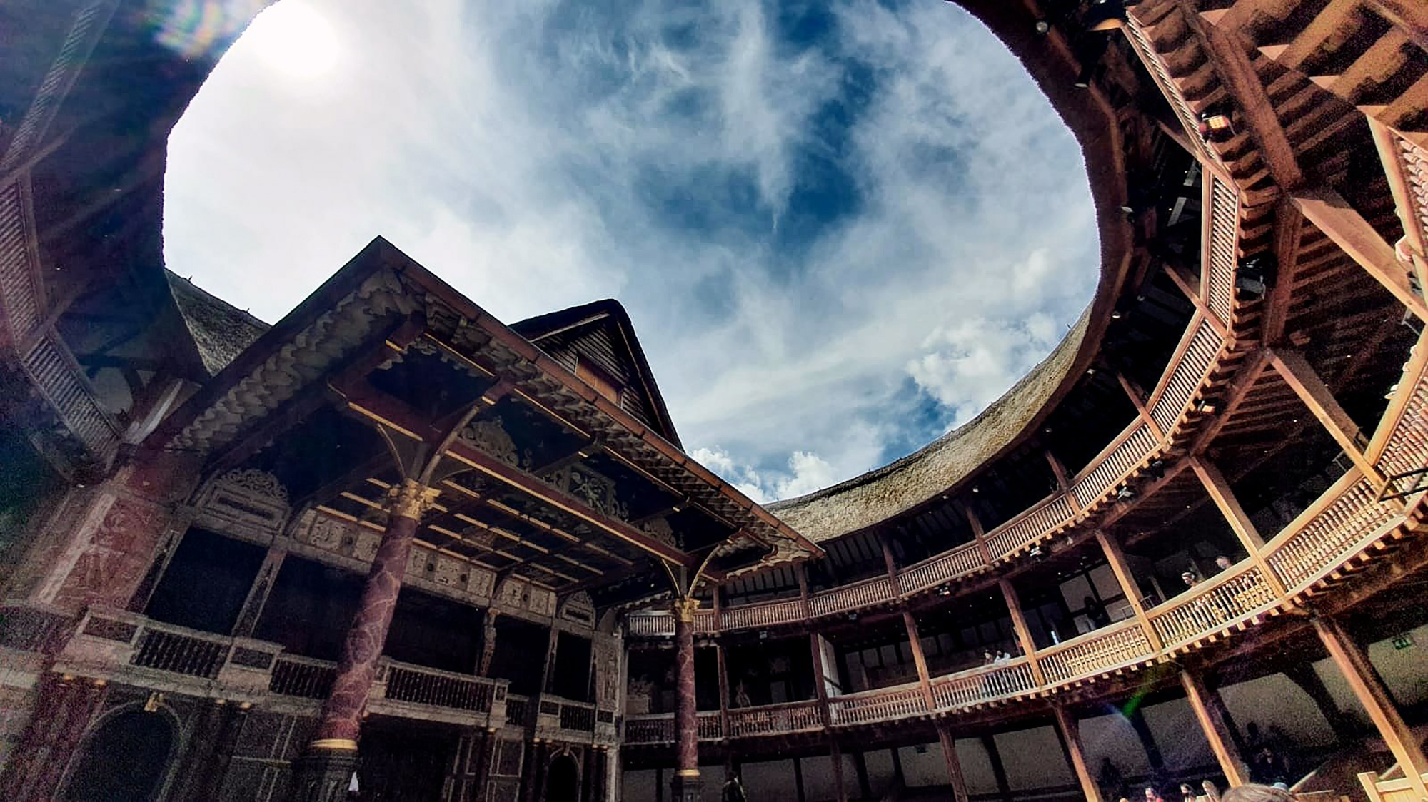 Shakespeare's Globe Theatre Open Air A blue sky streaked with wisps of white cloud above the circular timbre structure of the Globe Theatre.