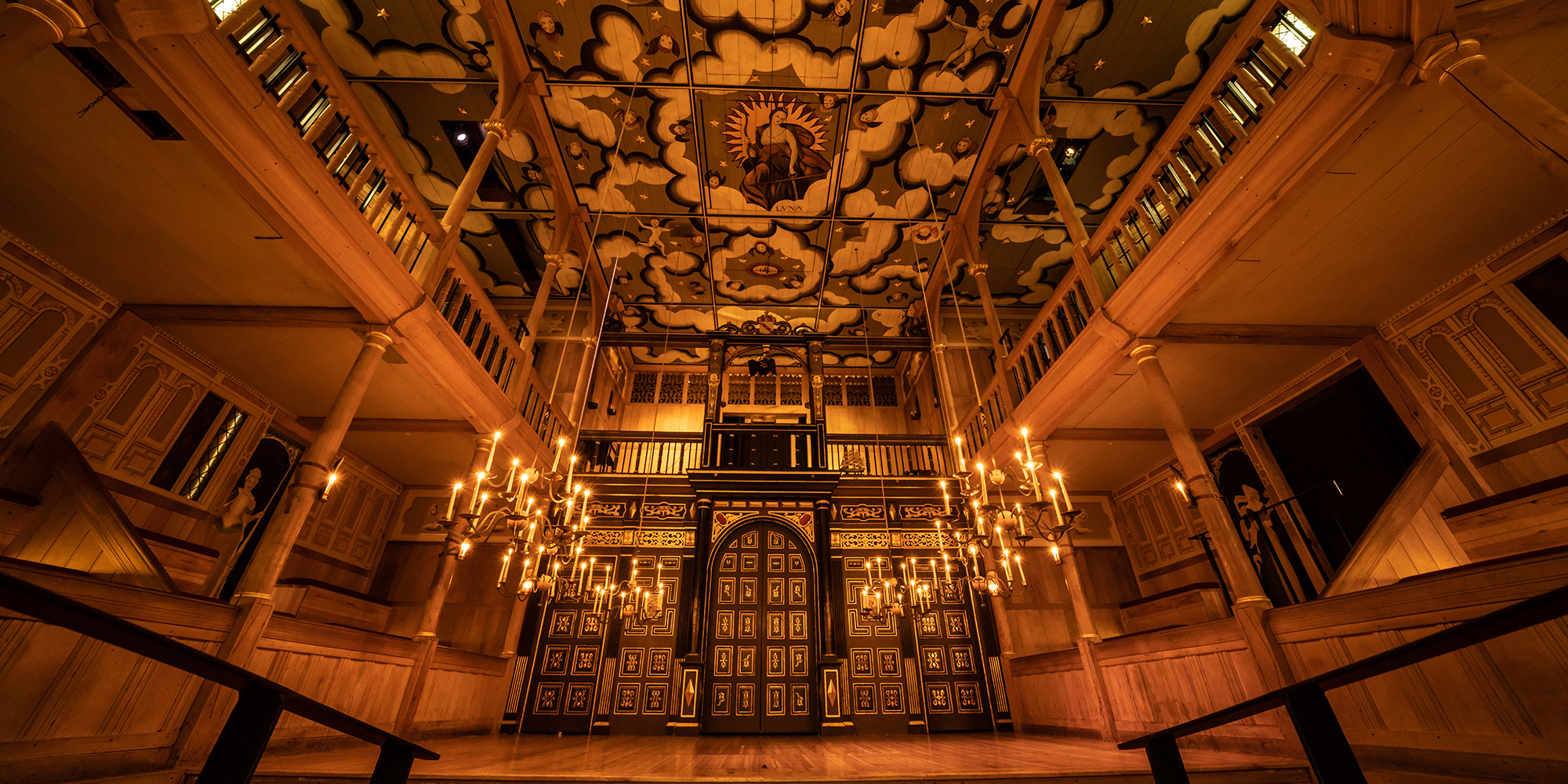 Sam Wanamaker Playhouse 2021 Flush Johan Persson A wide angled shot of the Sam Wanamaker Playhouse with its ornate painting ceiling depicting the Goddess Luna and clouds, hanging candelabra, and panelled painted doors.