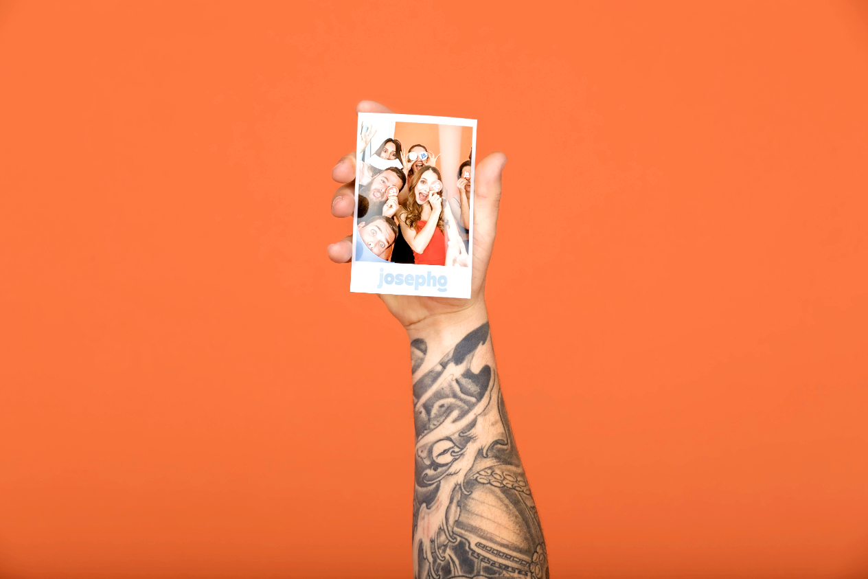 Une main d’homme tient une photo imprimée par la borne photo Josepho. Sur la photo nous voyons un groupe d’amis qui s’amusent et rient ensemble.