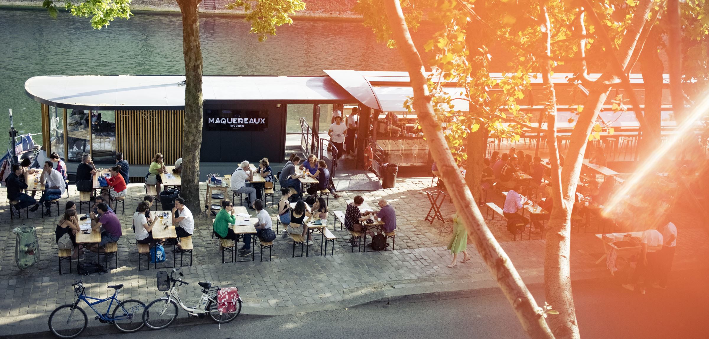 La terrasse du bar Les Maquereaux, au bord de la Seine, avec des personnes qui y boivent un verre.