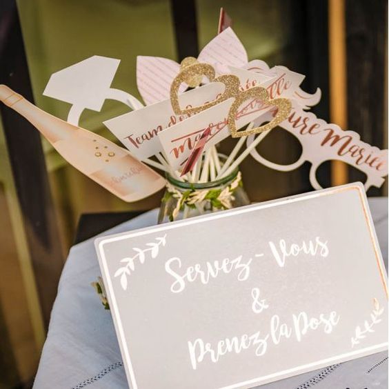Sur une table sont positionnés des accessoires pour prendre des photos fun avec un photomaton avec une pancarte qui dit "Servez vous et prenez la pose".