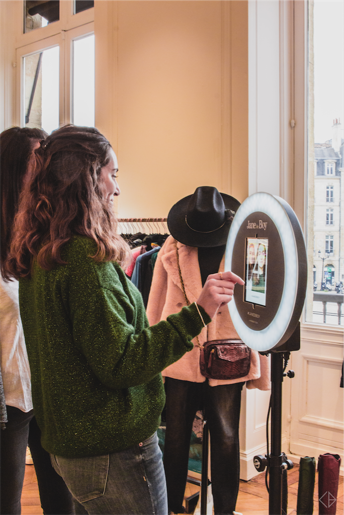 Une femme se prend en photo avec le photobooth de Josepho qui est positionné dans la boutique Jane de Boy et personnalisé avec les couleurs et le logo Jane de Boy.