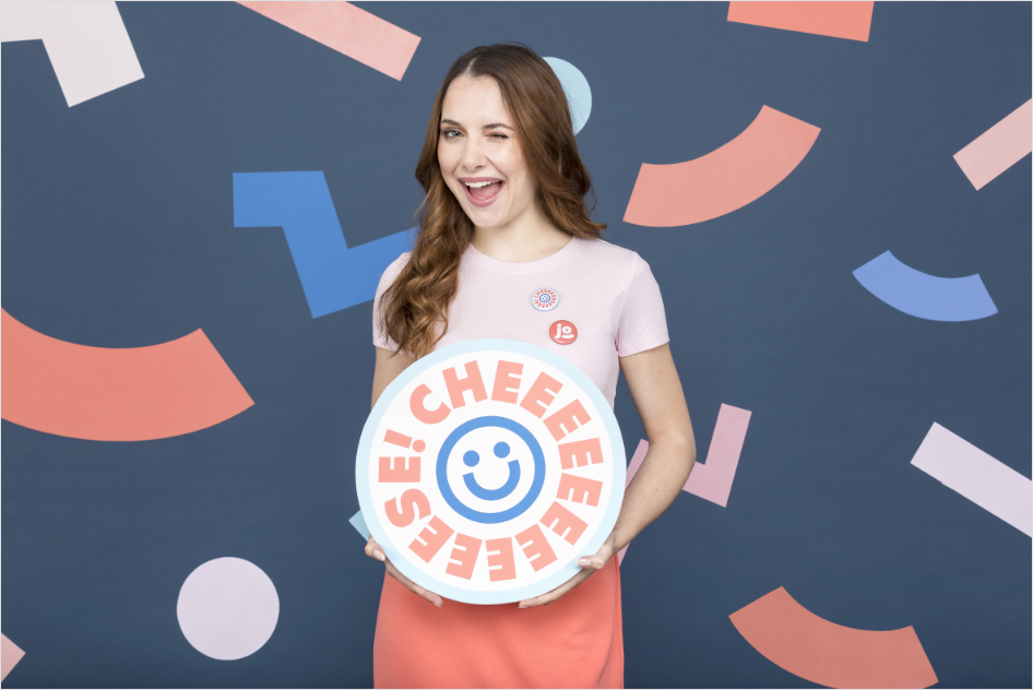 Une femme fait un clin d'oeil et tient dans les mains une pancarte ronde où il est écrit "cheese !" avec un smiley.