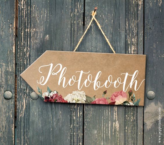 Une pancarte où est ecrit le mot "Photobooth" est attachée sur un mur en bois et indique l'endroit où se trouve le photobooth.