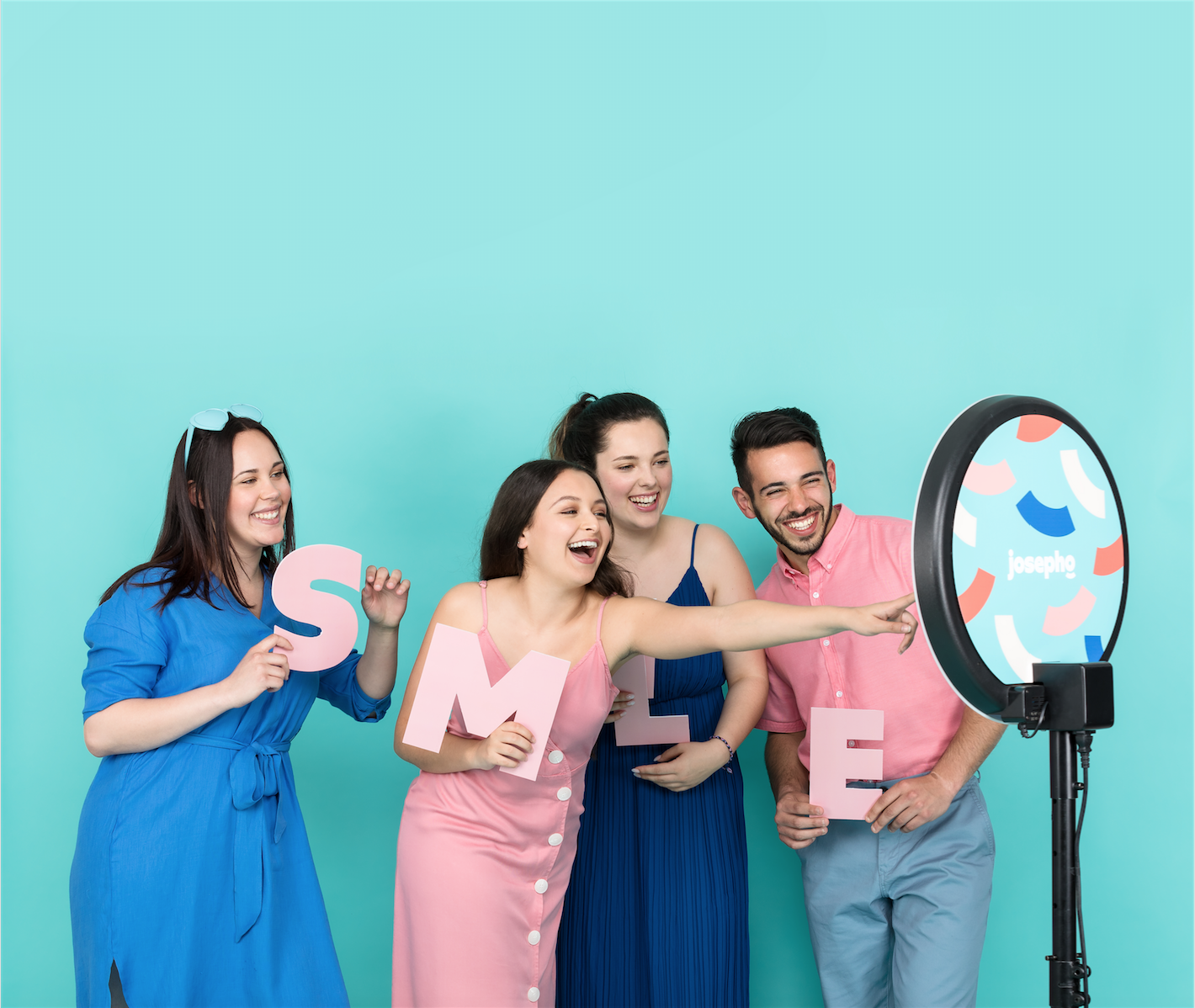Quatre amis se prennent en photo devant le photobooth en rigolant et en tenant chacun une lettre pour créer le mot "Smile".