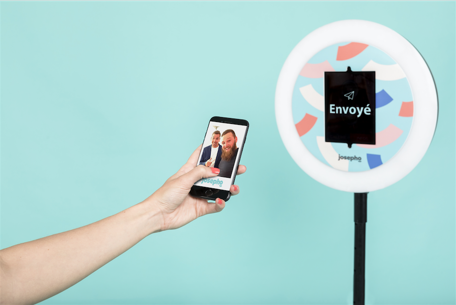 Le photobooth de Josepho est de face avec le message "envoyé" inscrit sur l'écran. Au premier plan une main tient un smartphone avec, sur son écran, la photo de deux amis prise avec le photobooth de Josepho.