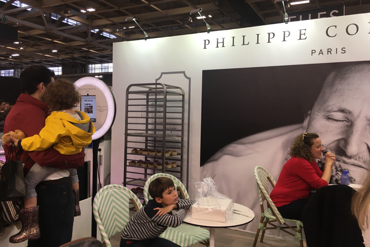 Sur le Salon du Chocolat, un père avec son enfant des les bras se prend en photo avec le photobooth de Josepho qui est personnalisé avec le logo Philippe Conticini.