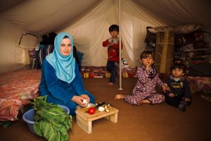 Ala's wife prepares food as the children play behind her. The family received food aid from Samaritan's Purse and World Food Programme.