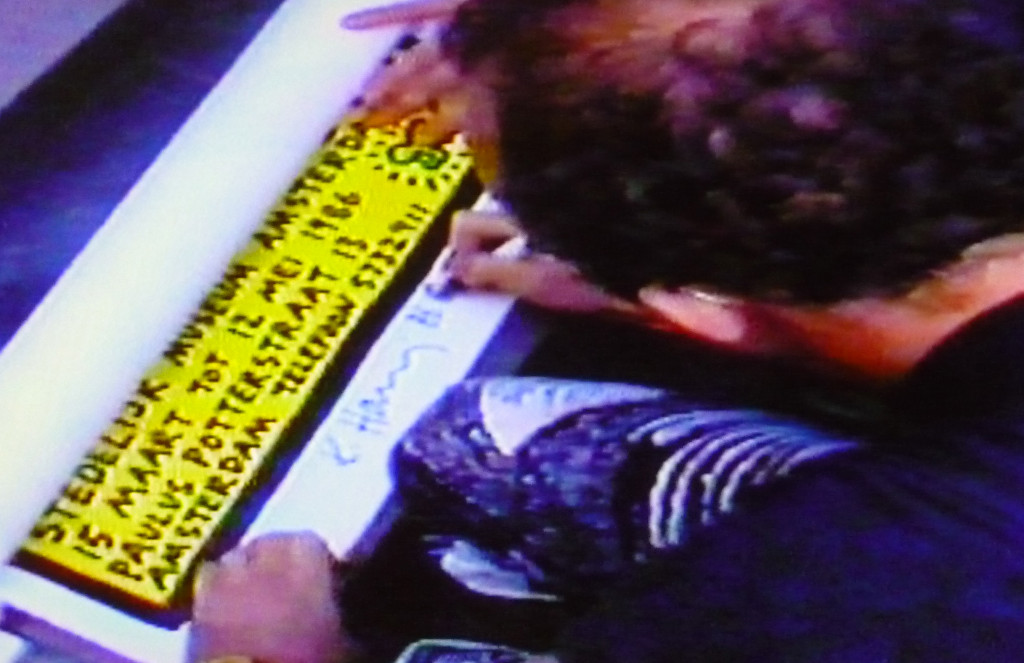 Keith Haring signing a poster after his lecture and tv-interview, Stedelijk Museum, Amsterdam, 15 March 1986; local TV Photo still: Chris Reinewald.