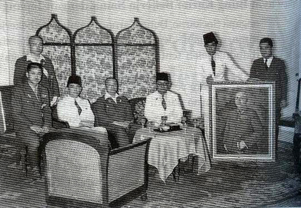 Meeting with Japanese officials, including General Imamura (seated, center), with Sukarno in Jakarta. The painter Basoeki Abdullah is holding the painting being presented, Portrait of General Imamura, 1942. Source: Aiko Kurusawa