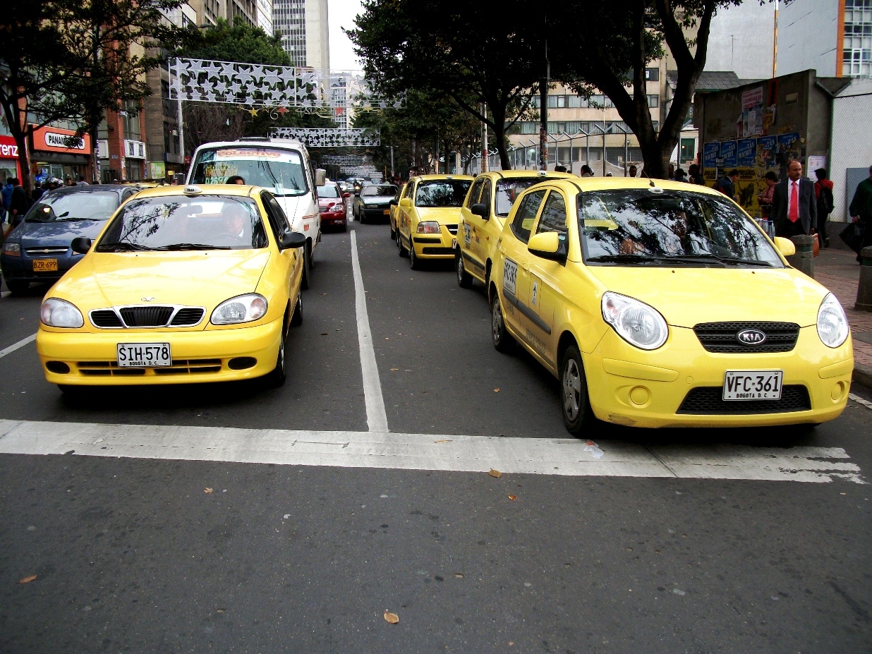 An avenue with taxis and other cars, starts decorations, trees, people. SmartExpat