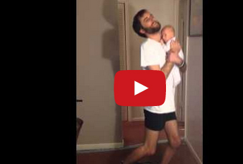 شاهد..  أب يرتدي البنطال بينما يحمل طفله الرضيع