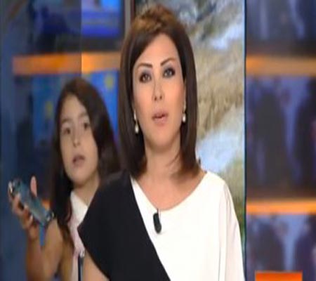 طفلة تدخل الاستوديو لتعطي والدتها الهاتف النقال أثناء قراءتها النشرة الإخباري