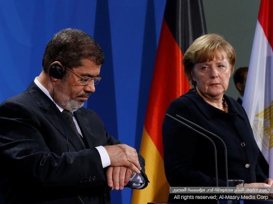 مرسي ينظر في ساعته أثناء حديث ميركل ( صور )