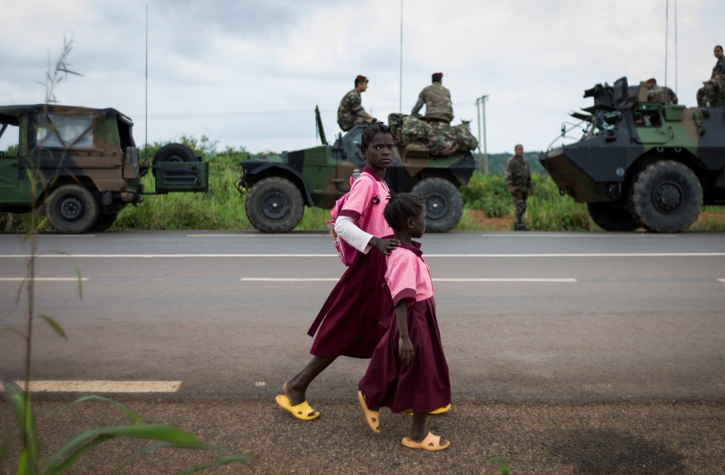 Kinderen lopen over straat, met op de achtergrond Franse militairen.