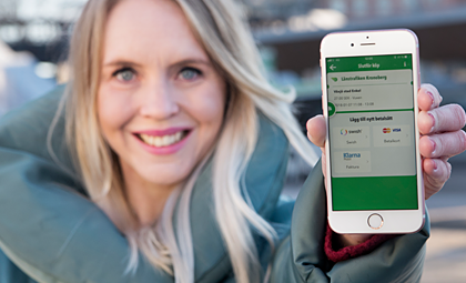 Illustrativ bild: Blond kvinna håller upp en smarttelefon. Telefonen visar ett utsnitt av vår reseapp.