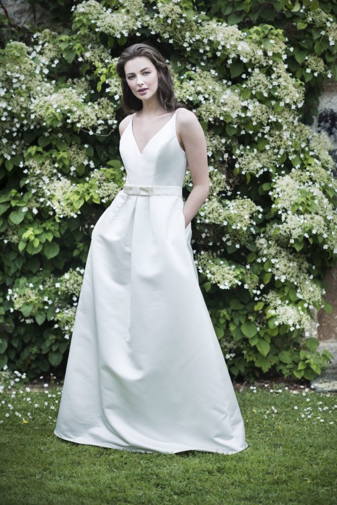 Bride in simple a-line dress against greenery.