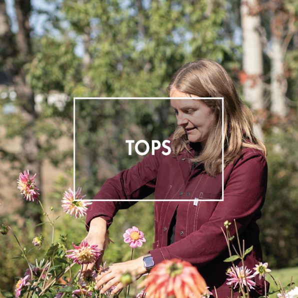 A smiling woman wearing a green work wear jacker infront of tomato plants.