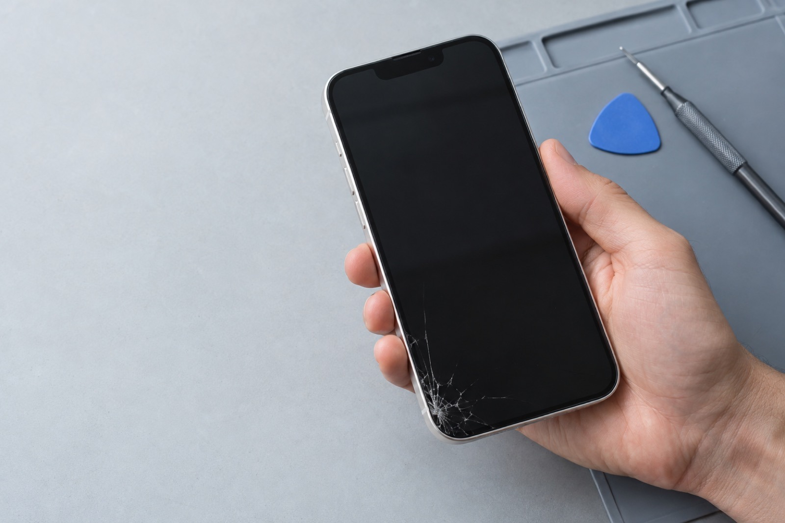 Illustration av en iPhone med sprucken skärm vid en reparationsbänk
