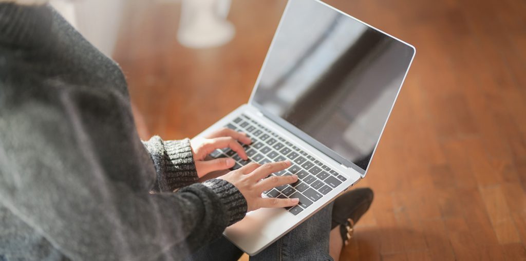 Nainen istuu lattialla kannettava tietokone sylissään