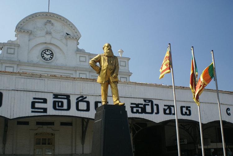 Colombo Fort Railway Station statue at the front with flag poles flying the Sri Lankan Flag Colombo Fort Railway Station