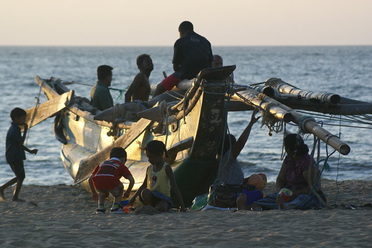 Local families come out to watch the sunset on Negombo Beach and sit around a fishing boat in Sri Lanka Negombo beach fishing boats