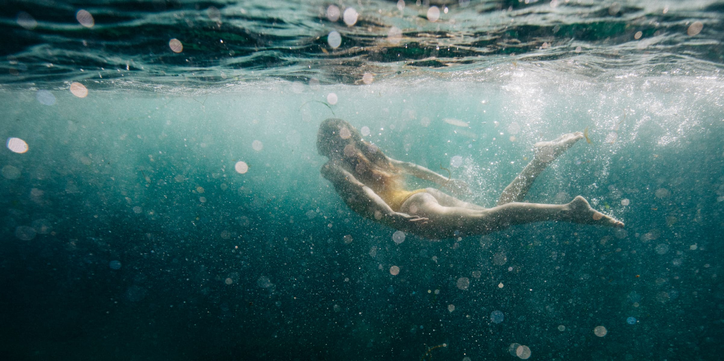 An underwater image of a woman with long hair in a yellow swimsuit in the sea.