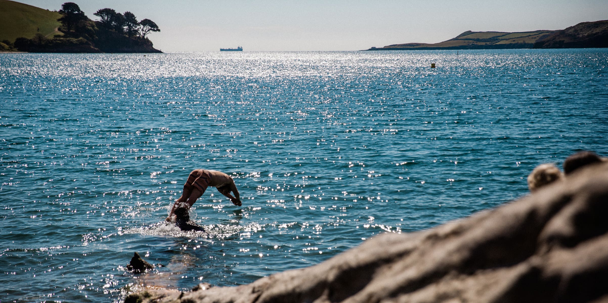 A person diving in the sparkling blue sea on the Cornish coast.