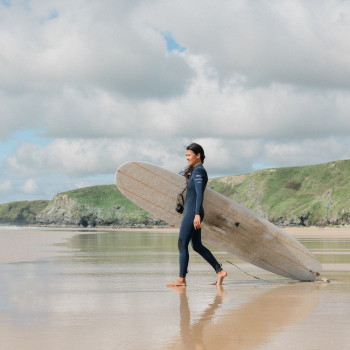 A woman carrying a surfboard heads across the sand to the sea