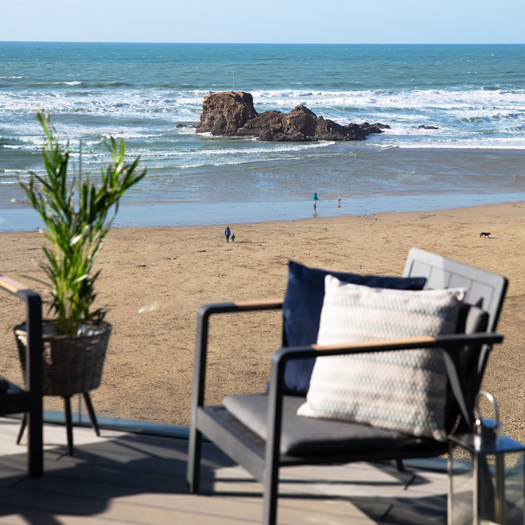 Ein Stuhl und eine Pflanze auf einer erhöhten Holzterrasse mit Blick auf Strand und Meer im Hintergrund.