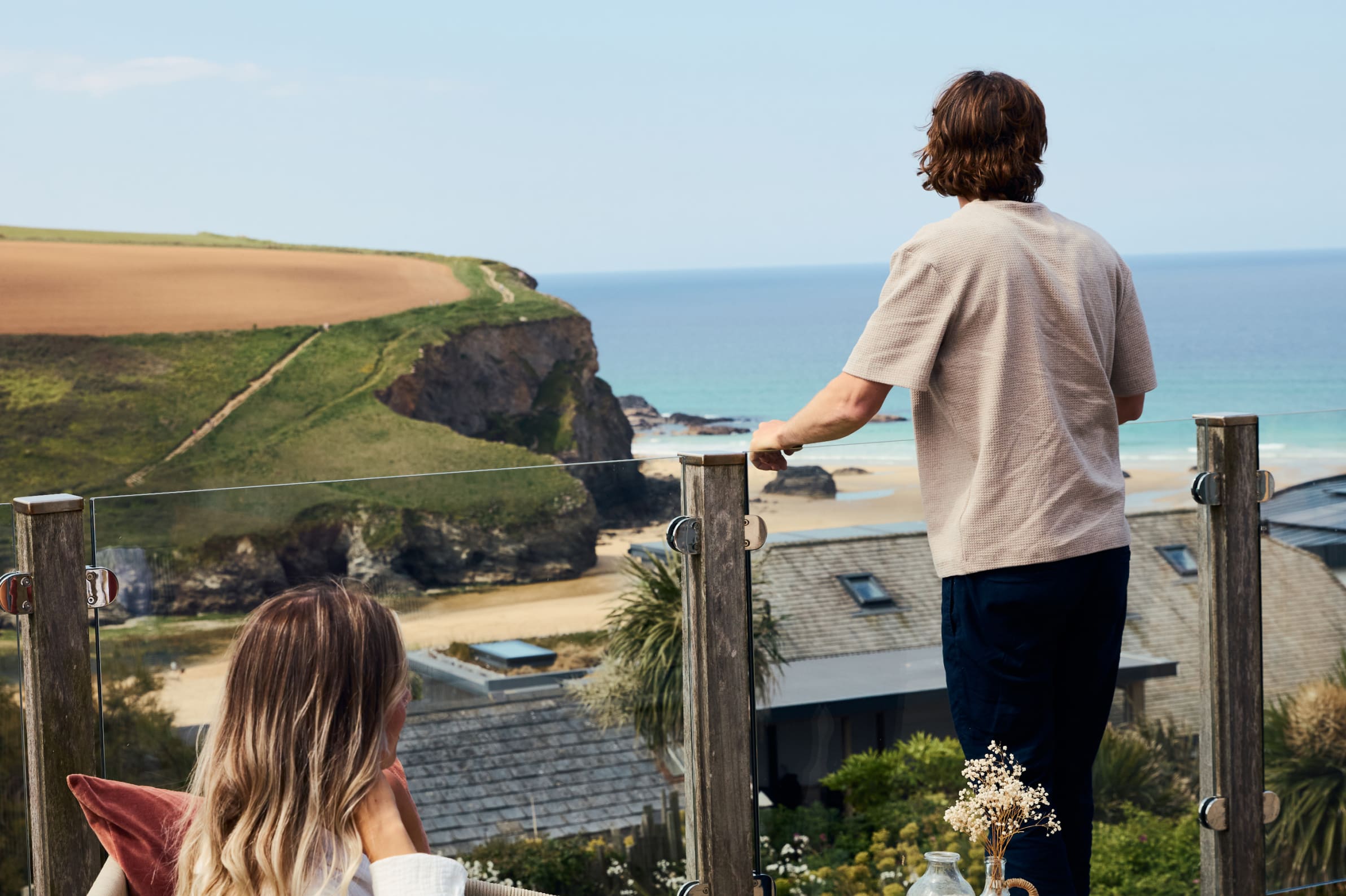 A man with brown hair looking out towards the sea from a property balcony.