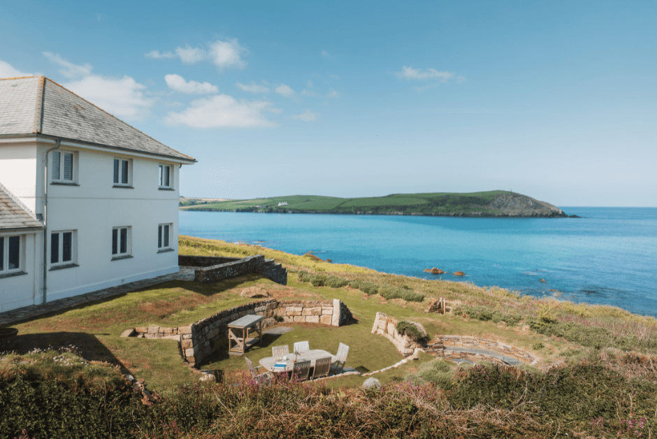 A large house with an outdoor dining area right on the coast, with views over the sea and headland.  