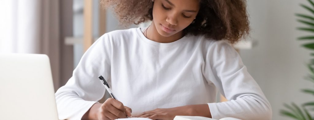 Ein Mädchen sitzt am Schreibtisch und macht Notizen