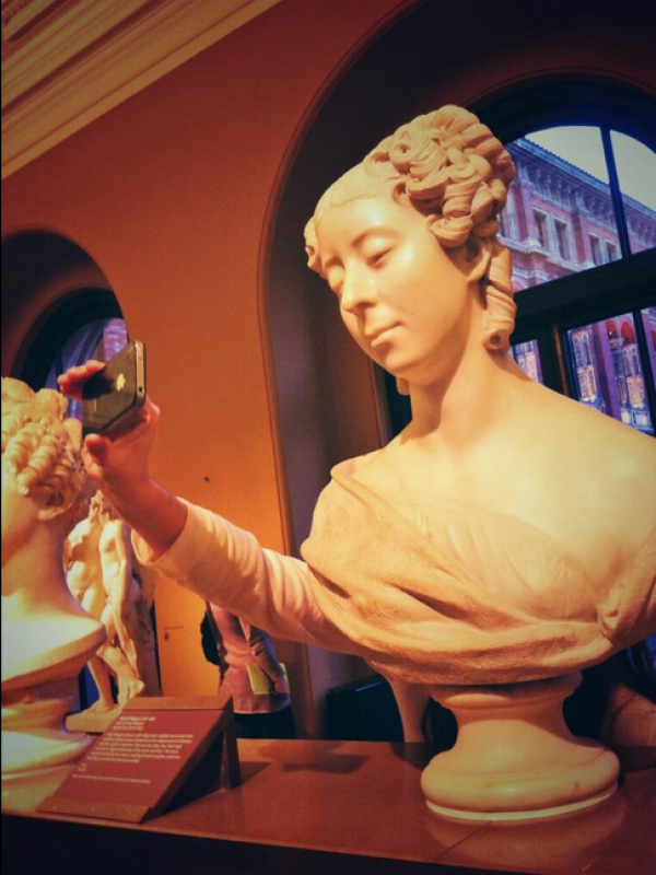 A bust in the sculpture gallery takes a museum selfie