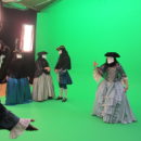 A cast in costume filming in front of a green screen