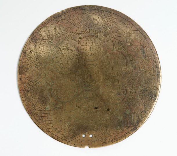 A close up of the engraved astrological disk which depicts the twelve zodiac signs, magic squares, a section of Al-Asma' al-Husna (Beautiful names of Allah), and the dot and lined figures created using the ilm al raml technique as seen in the first image. The two small holes at the bottom indicate the possibility of a handle attached to this object at some point in the past. © Victoria and Albert Museum
