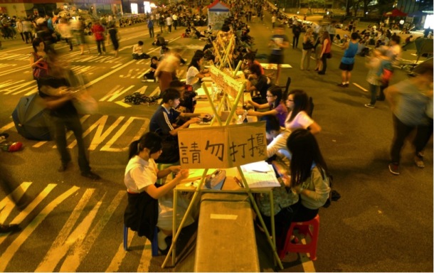 Study corner in early October, designed by teachers and students from the Polytechnic University. The workstations were built along a concrete road barrier on Connaught Road, Admiralty, adapted from salvaged wood planks and stools from around the site. The study corner has been expanding ever since. Photograph by Becky Sun. ©Becky Sun.