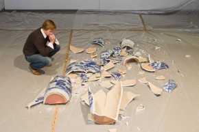 A man crouches by a pile of smashed blue and white ceramic pieces