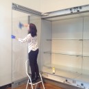 Curator Rebecca Wallis stands on a stepladder cleaning the wall case