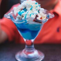a glass cup with ice cream and blue bubblegum flavoured topping sauce