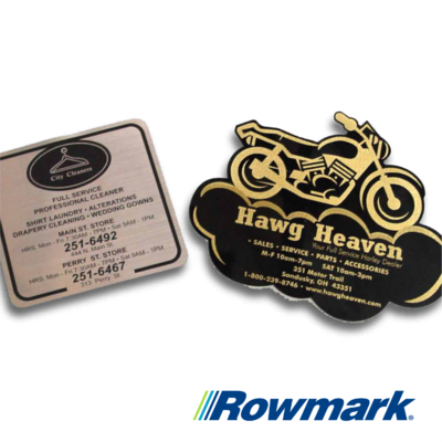Two custom engraved signs made with Rowmark materials, including a metallic cleaner service plaque and a gold-on-black motorcycle-shaped Hawg Heaven sign.