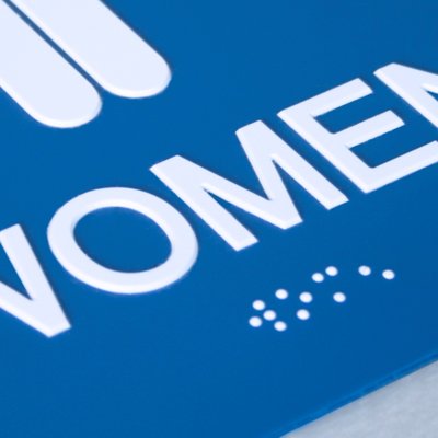 Blue tactile sign with raised white text reading “WOMEN” and Grade 2 braille for accessibility
