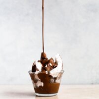 chocolate sauce drizzling over ice cream in a glass bowl
