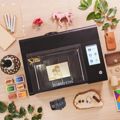 FLUX beamo desktop laser cutter in use, surrounded by engraved crafts and materials
