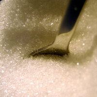 a pile white sparkling shiny granulated sugar with a metal spoon