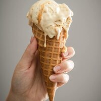 a hand holding a waffle cone with melting ice cream and butterscotch topping sauce. 