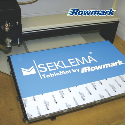 Laser engraver with a blue Seklema TableMat by Rowmark holding material in place on the worktable.