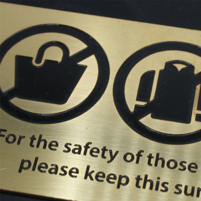 Engraved brass sign with black safety icons and text warning for public safety.